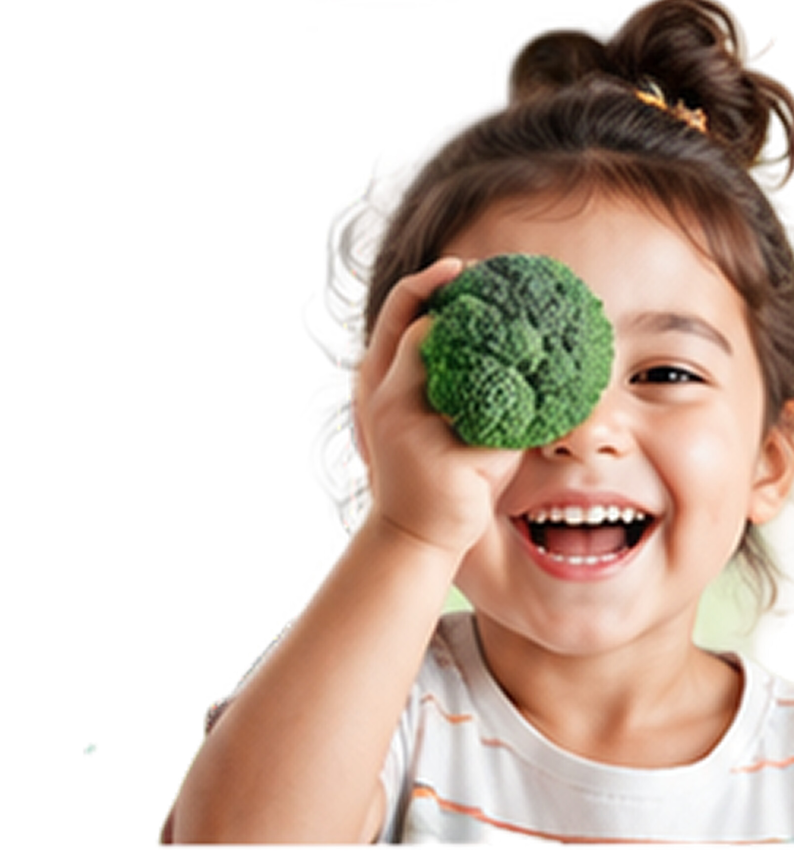 A smiling child holding a piece of broccoli up to one eye